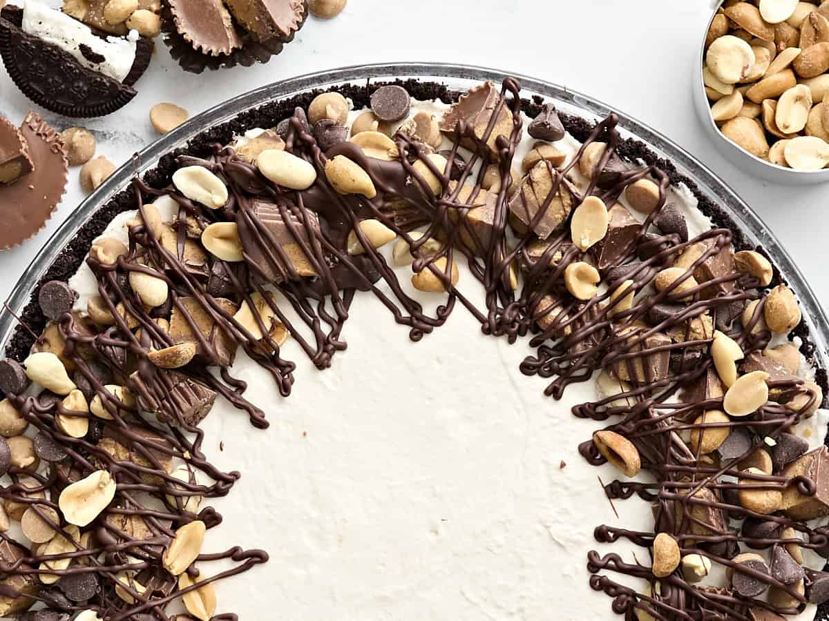 Gros plan d'une tarte au beurre de cacahuète décorée de chocolat fondu, de cacahuètes et de coupes de beurre de cacahuète hachées.