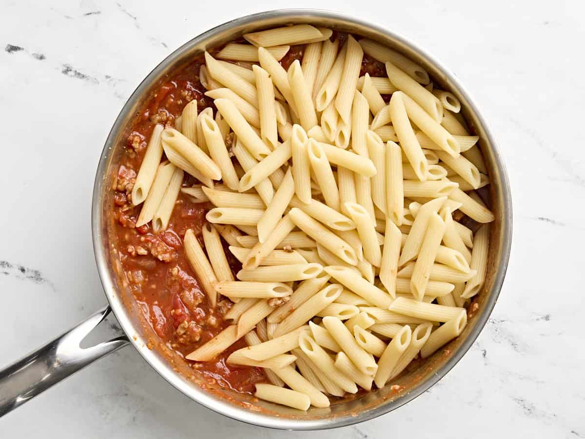 Pâtes cuites ajoutées à la sauce à la viande dans une poêle.