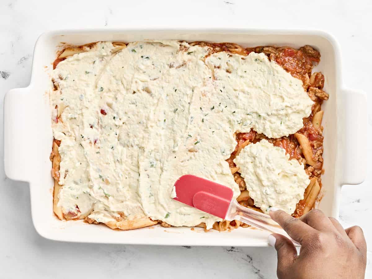 Mélange de fromage étalé sur la sauce pour pâtes dans un grand plat allant au four.