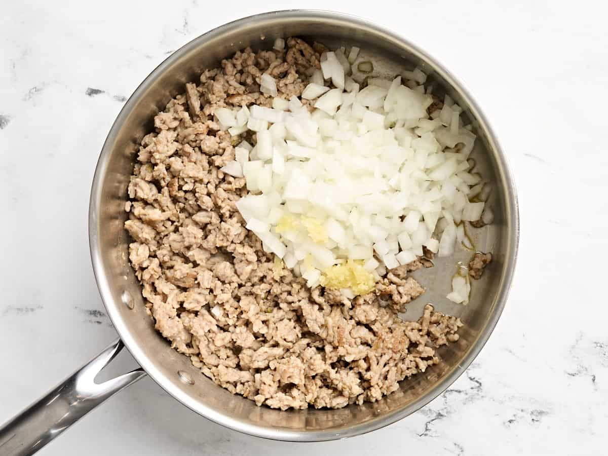 Oignon et ail coupés en dés ajoutés à la poêle à saucisses.