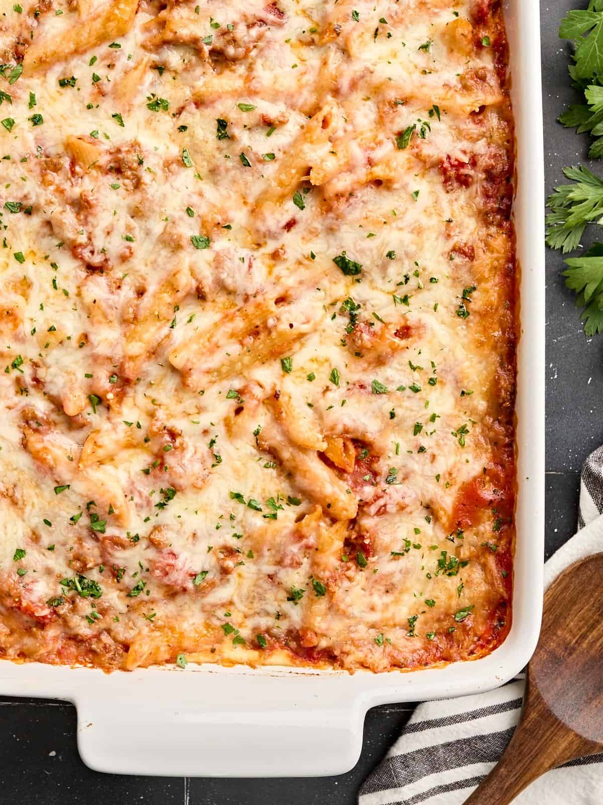 Vue aérienne des mostaccioli cuits au four avec une cuillère de service en bois sur le côté.