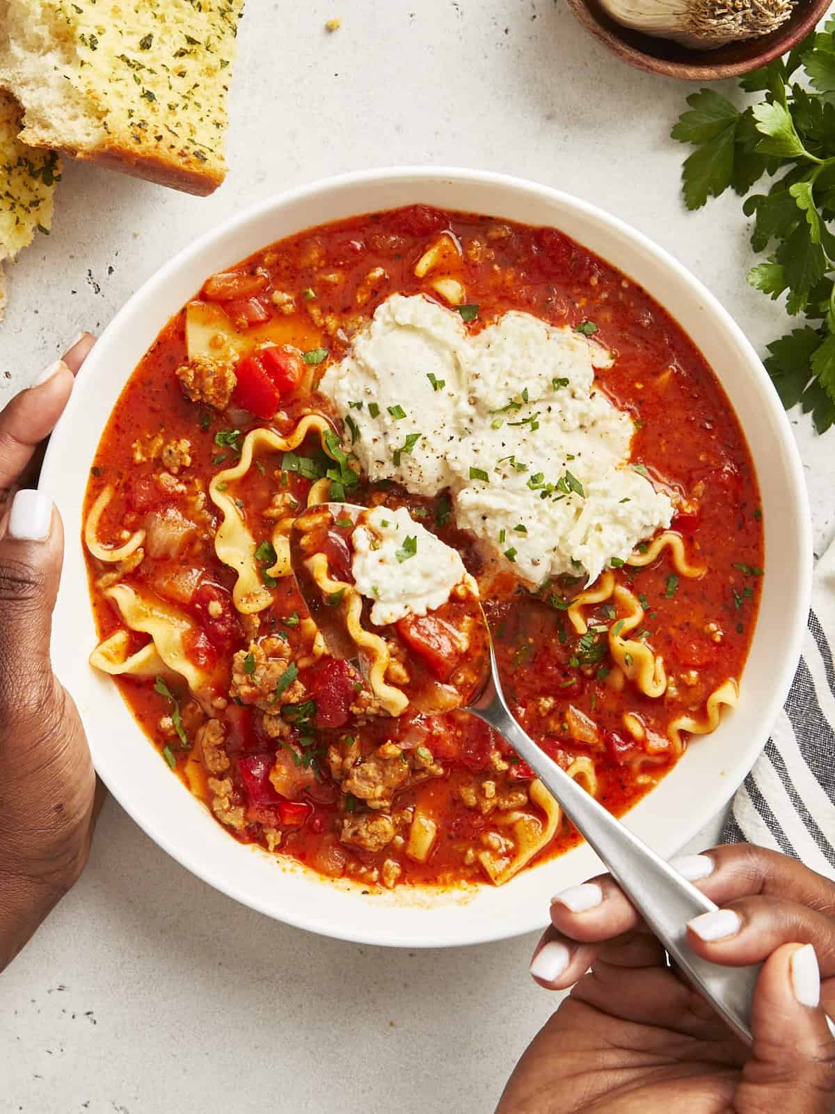 Vue aérienne de la soupe aux lasagnes dans un bol blanc avec une main tenant une cuillère en soulevant un peu.