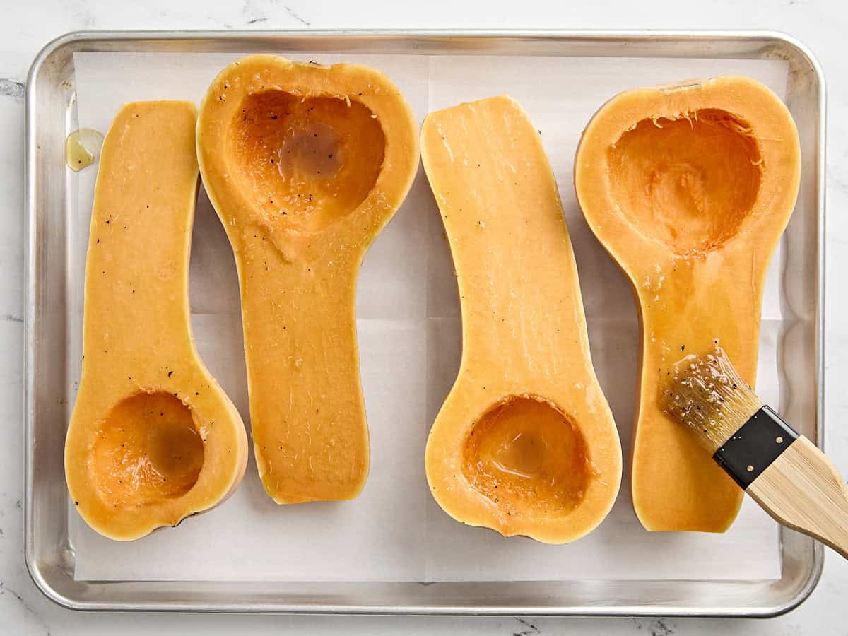 2 courges musquées coupées en deux sur une planche à découper en bois badigeonnées de marinade à l'érable.