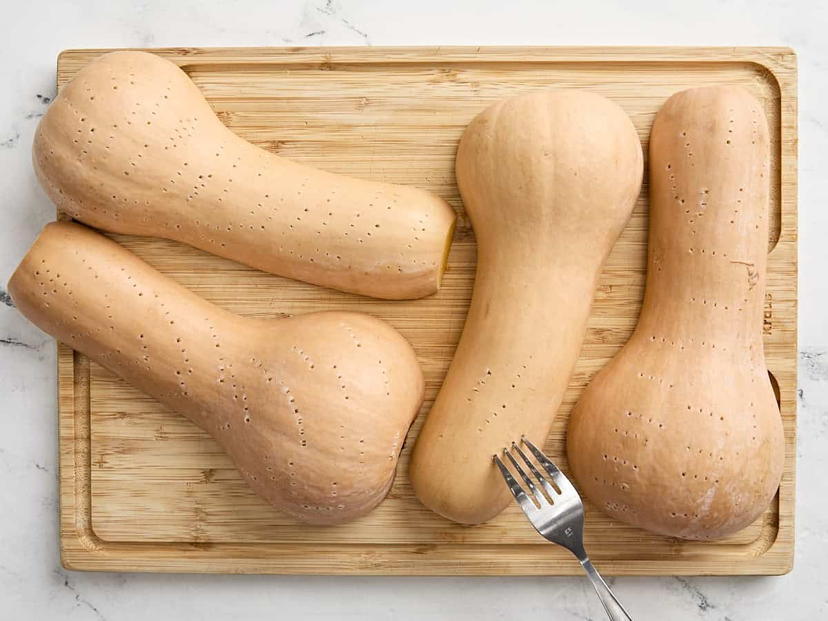 Une fourchette perçant un trou dans la peau de 4 courges musquées coupées en deux sur une planche à découper en bois.