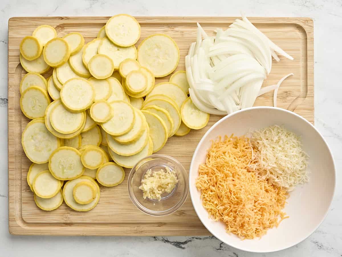 Courge tranchée, oignons, ail émincé et fromages râpés sur une planche à découper en bois.