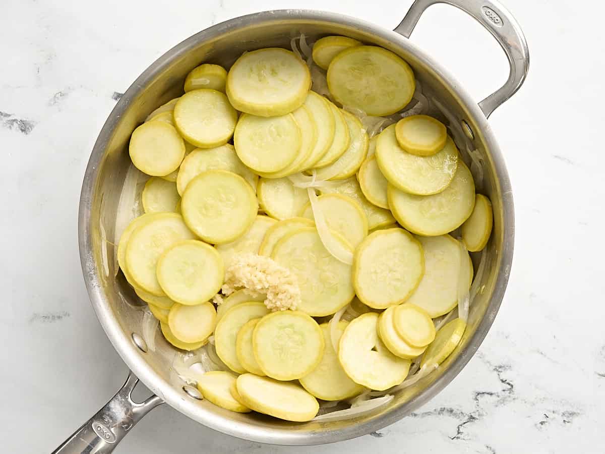 Courge jaune tranchée cuite dans une poêle avec des oignons et de l'ail émincé.