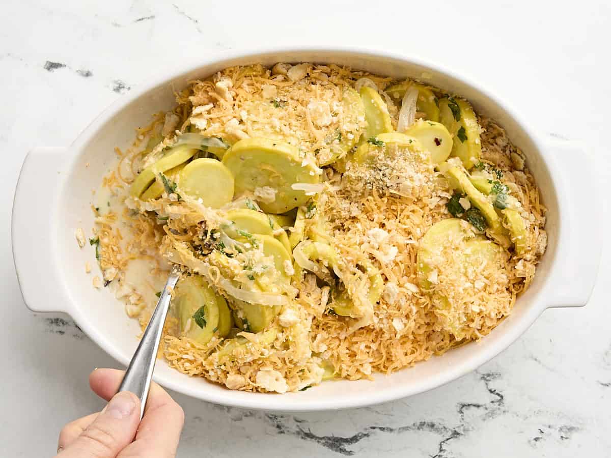 Une cuillère mélangeant les ingrédients de la cocotte de courge dans une cocotte.