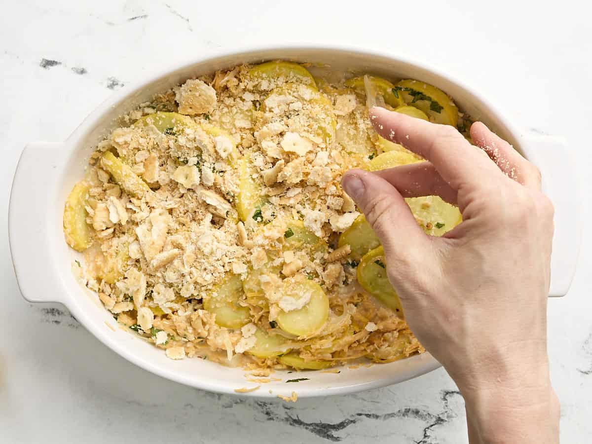Une main saupoudrant des craquelins Ritz écrasés sur une cocotte de courge dans une cocotte.