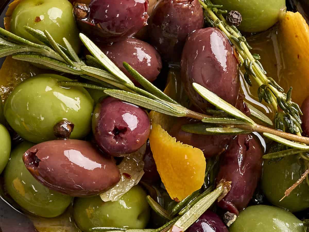Gros plan d'olives marinées et d'herbes fraîches.