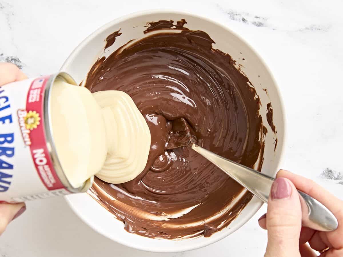 Lait concentré sucré versé dans un bol de chocolat fondu.