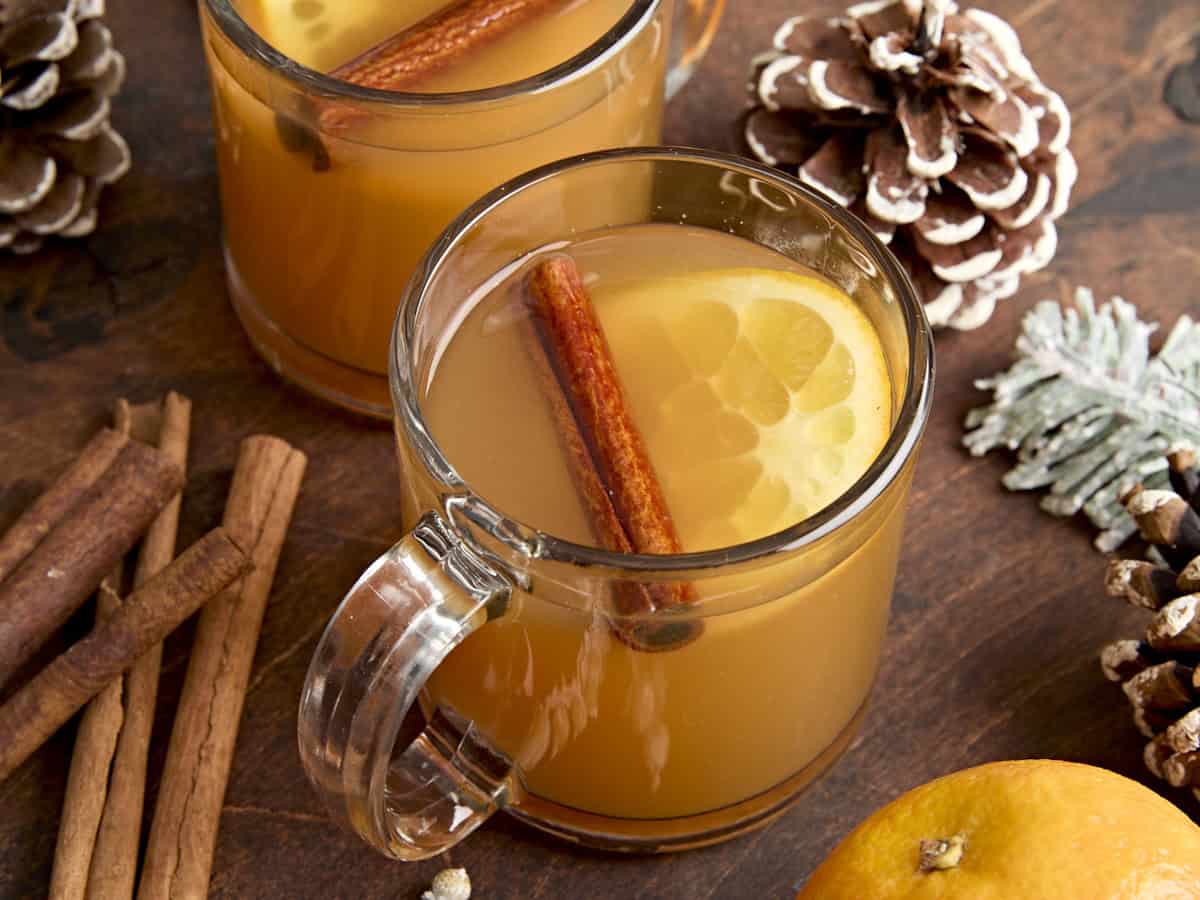 Vue latérale d'une tasse de cidre chaud, garnie d'un bâton de cannelle et d'une tranche d'orange.