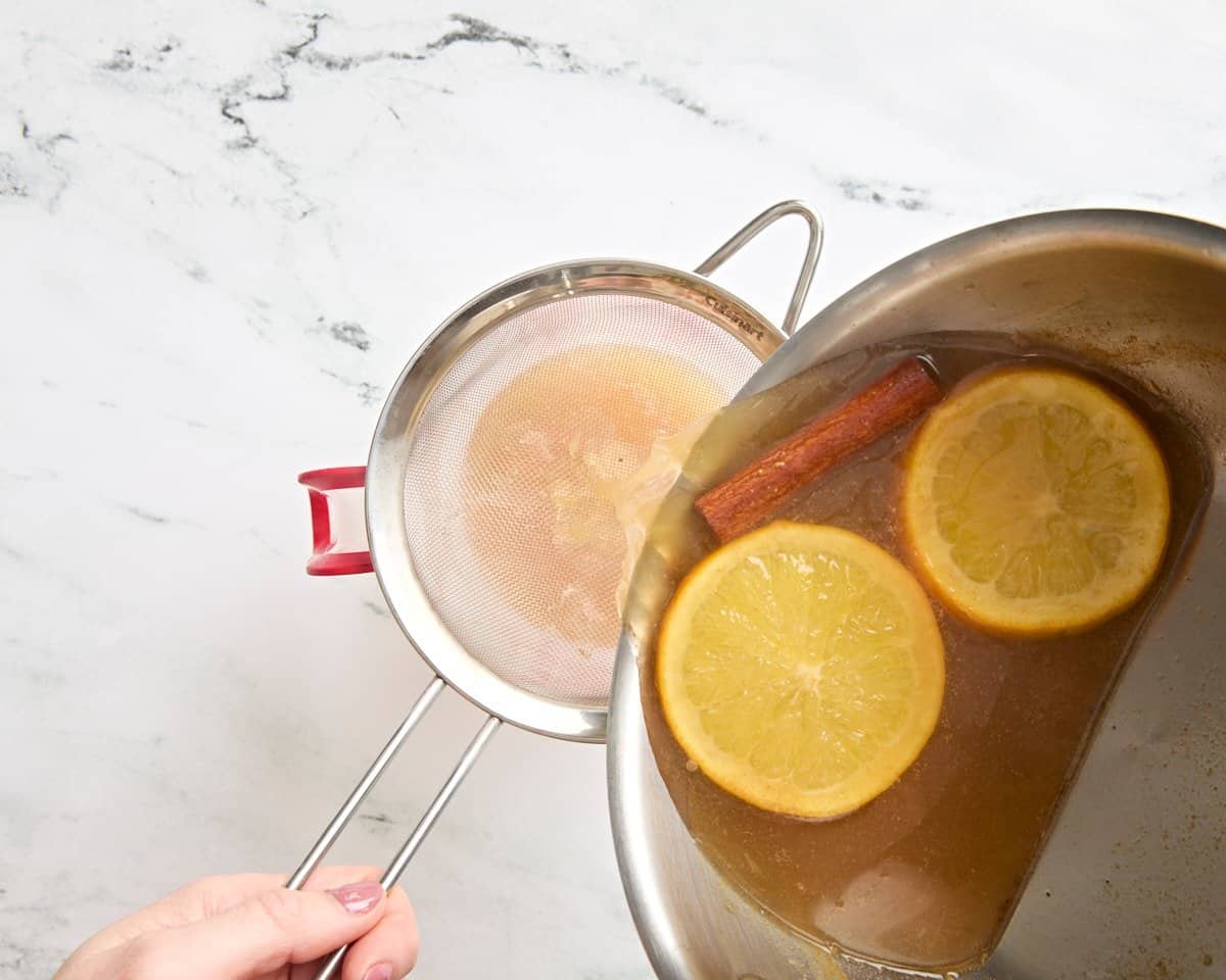 Cidre chaud versé dans une casserole dans une passoire.