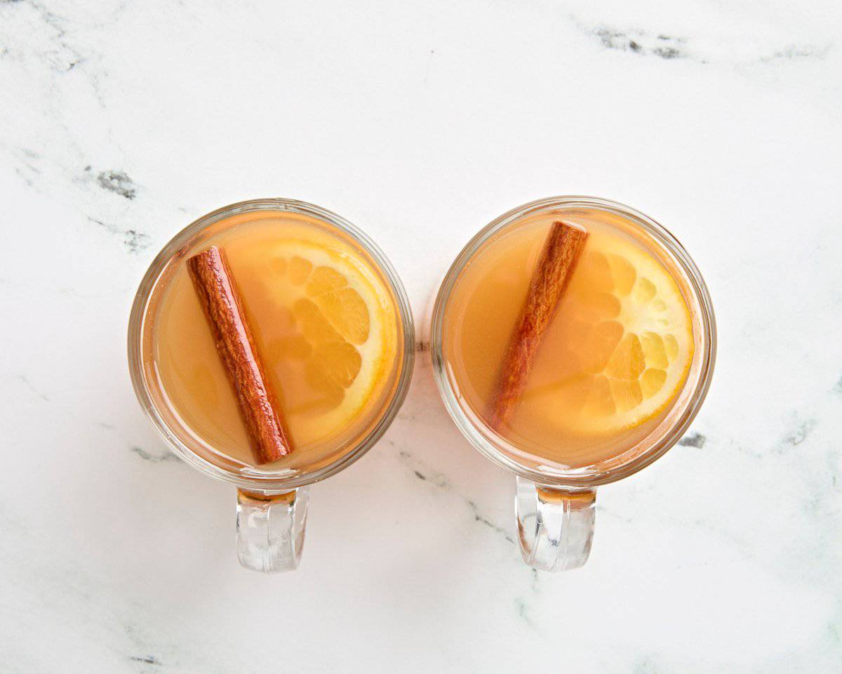 Vue aérienne du cidre de pomme chaud dans des tasses avec une tranche d'orange et un bâton de cannelle.