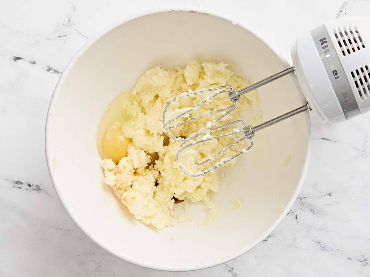Oeuf ajouté au mélange de beurre en crème et de sucre dans un bol à mélanger avec un batteur à main.