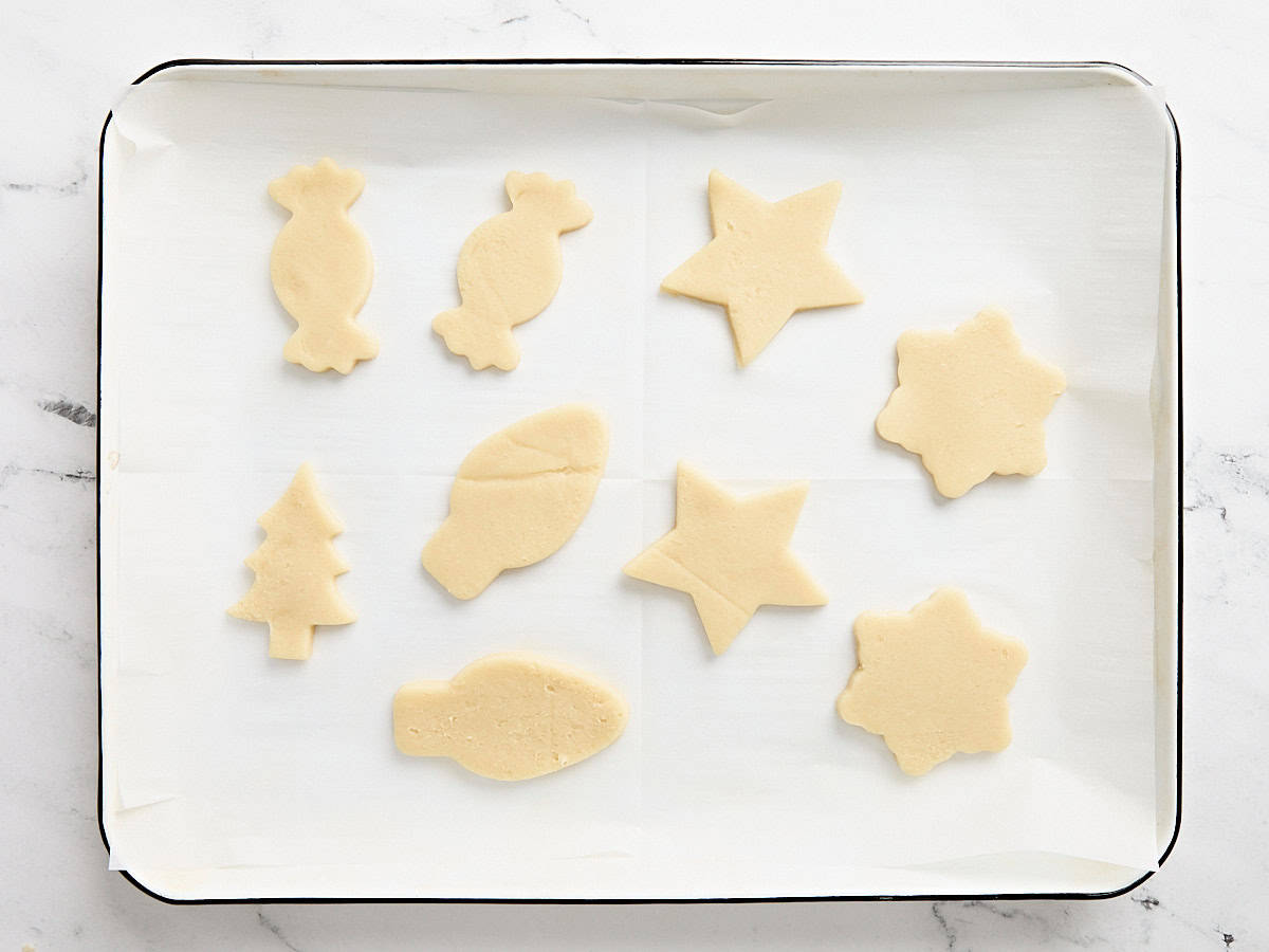 Découpez des biscuits au sucre festifs sur une plaque à pâtisserie tapissée de papier sulfurisé.