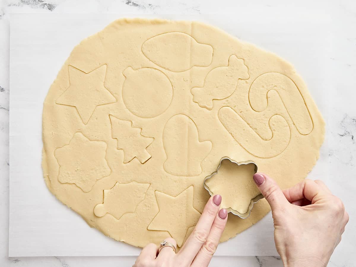 Une main découpant des biscuits au sucre festifs.