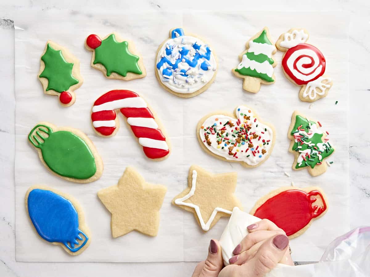 Une main tenant une poche à douille décorant des biscuits au sucre avec du glaçage royal.