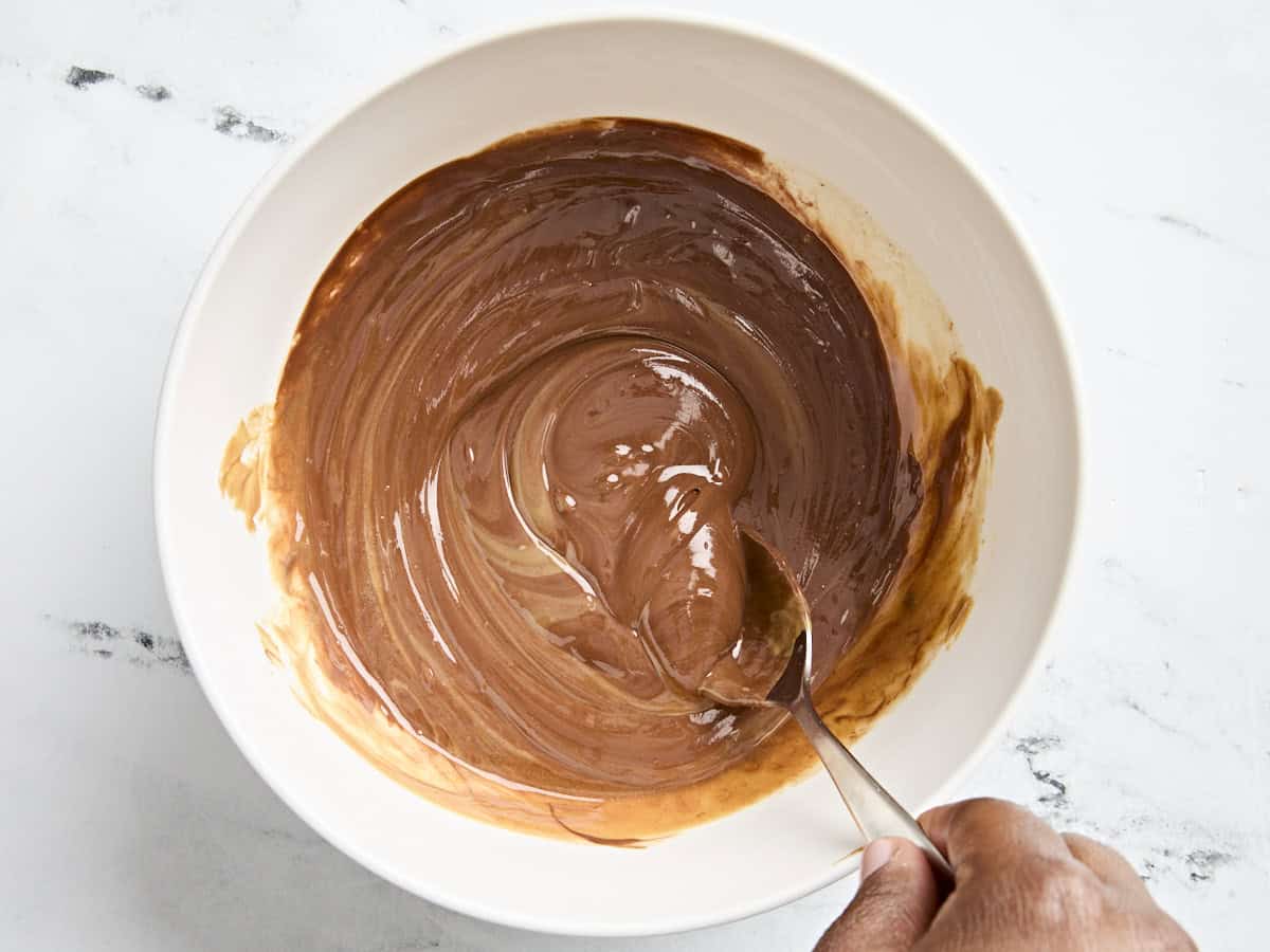 Chocolat fondu et beurre de cacahuète mélangés avec une cuillère dans un bol à mélanger.