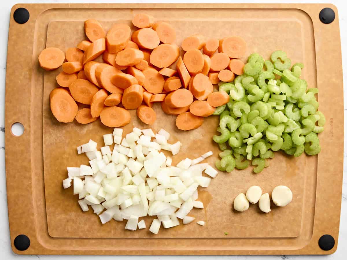 Mire poix et gousses d'ail émincées sur une planche à découper en bois.