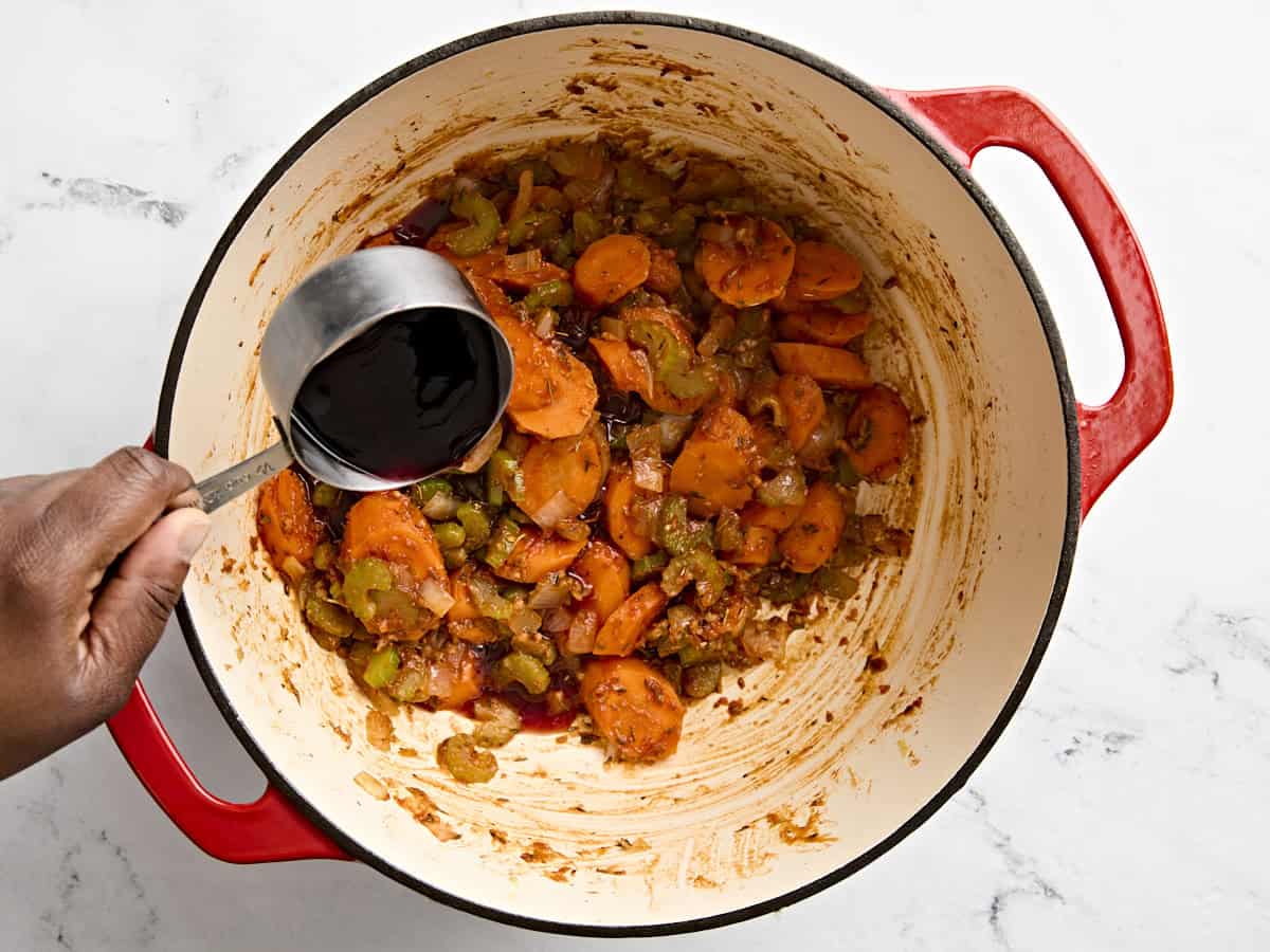 Vin rouge ajouté au ragoût de bœuf dans une cocotte.