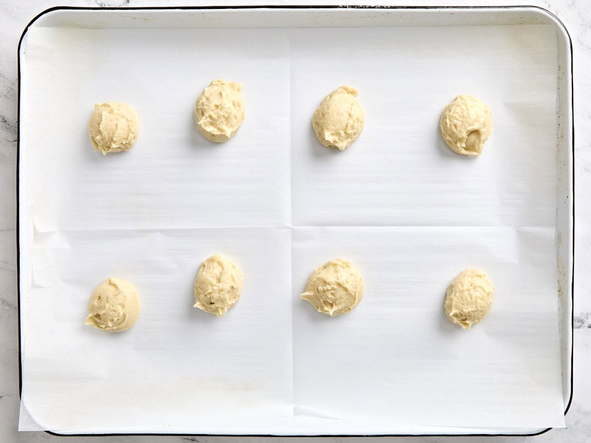 Des boules de pâte à biscuits noire et blanche sur une plaque à pâtisserie tapissée de papier sulfurisé.
