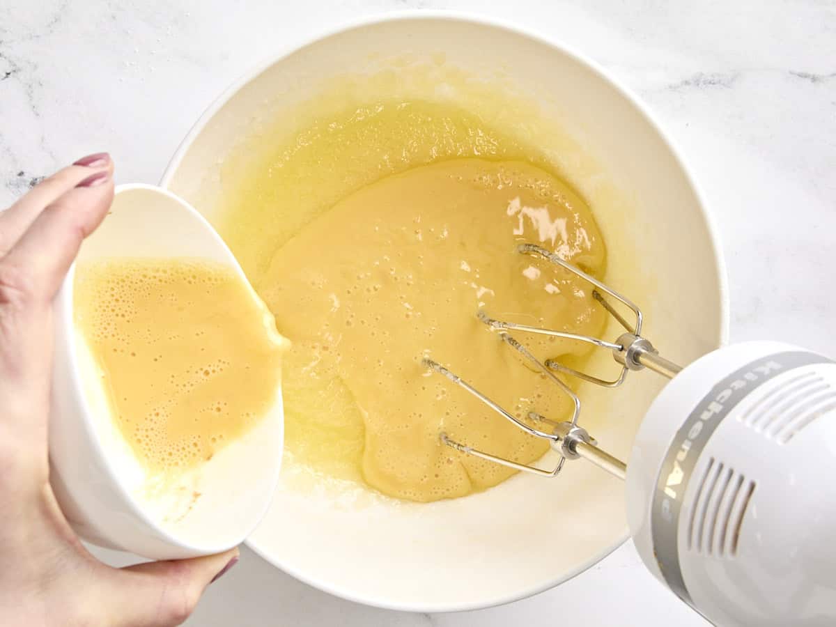 Œufs battus versés dans un mélange de beurre fondu et de sucre dans un bol.