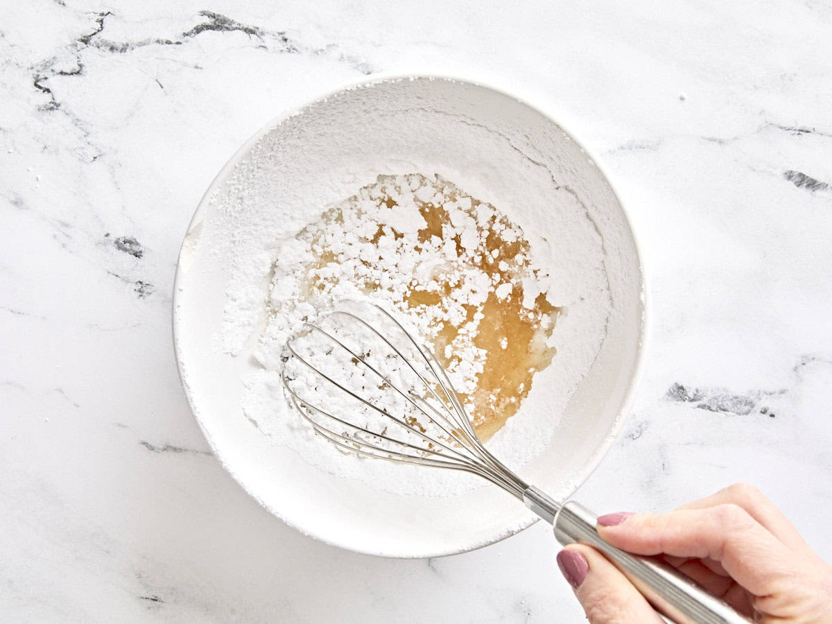 Le sirop de maïs, le jus de citron et l'eau chaude sont mélangés au sucre en poudre dans un bol.