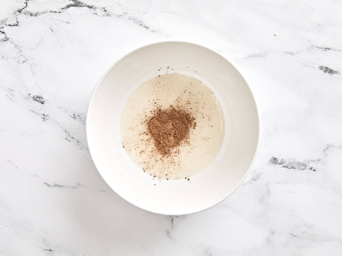 Poudre de cacao ajoutée au glaçage blanc dans un bol.
