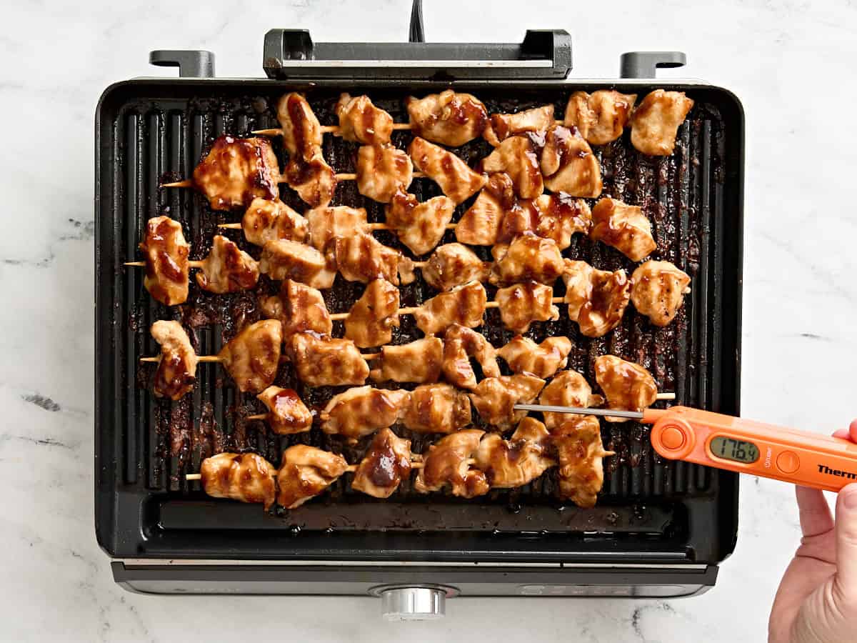 Un thermomètre à viande vérifiant la température interne des kebabs de poulet grillés sur un gril.