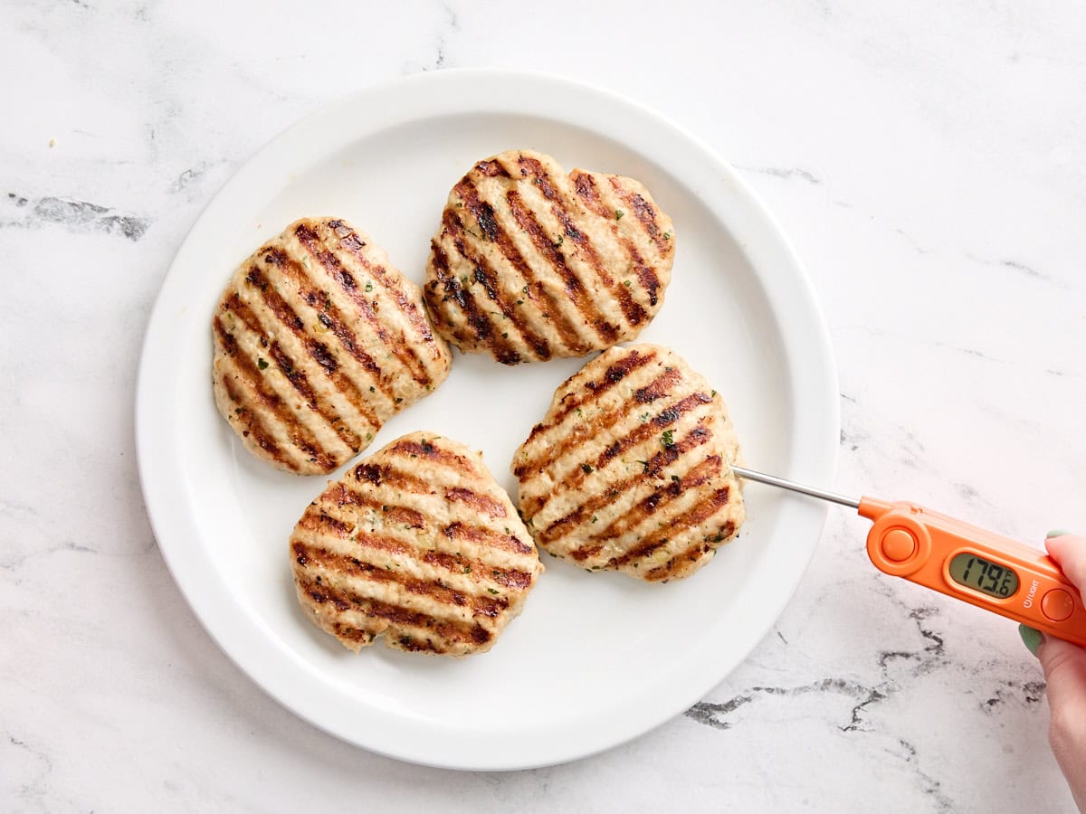 Un thermomètre à viande vérifiant la température interne des hamburgers de poulet grillés.