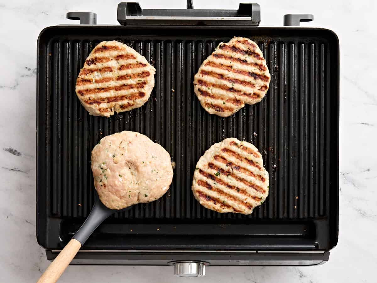 Une spatule retournant des hamburgers de poulet sur un gril.