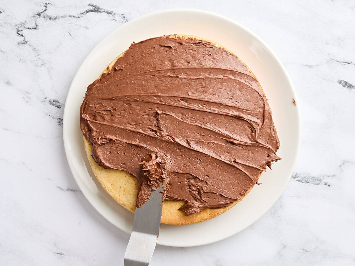 La crème au beurre au chocolat est répartie sur une couche d'un gâteau à la vanille maison.