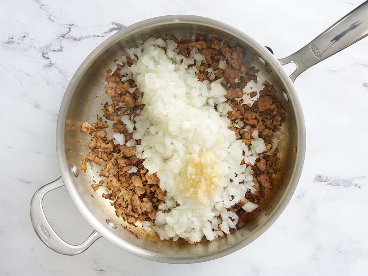 L'ail haché et l'oignon coupés en dés ajoutés à la saucisse dorée dans une poêle.