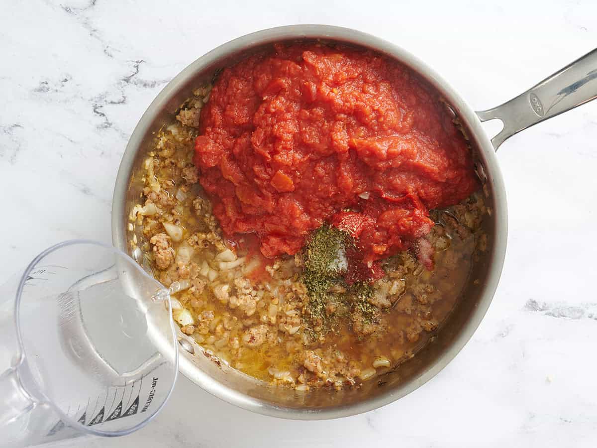 Les assaisonnements et la pâte de tomate ont ajouté à des saucisses cuites dans une poêle.