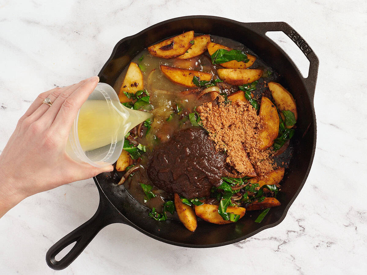 Le beurre de pomme, le bouillon de poulet et les assaisonnements ajoutés à une poêle avec des oignons et du chou vert.
