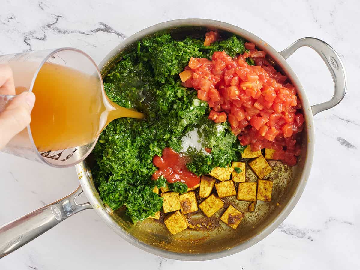 Les tomates en dés, le bouillon et les pâtes d'épinards ont ajouté à une poêle avec du tofu.