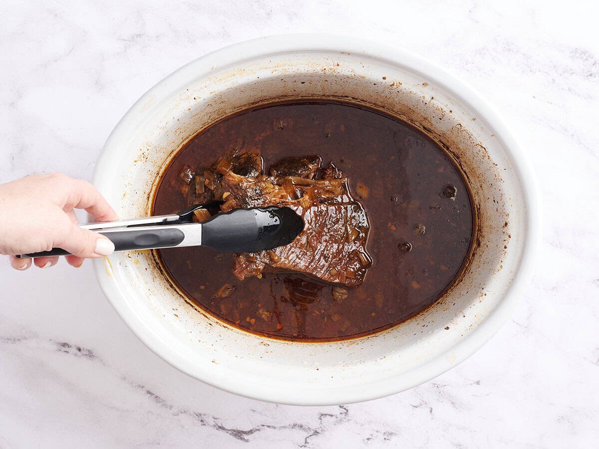 Un rôti de mandrin dans une mijoteuse avec des pinces de cuisine le soulevant légèrement.