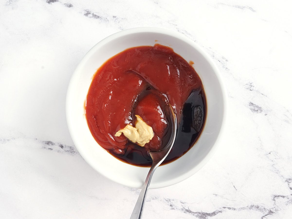 La moutarde de Dijon, le ketchup, la sauce soja et la cassonade sont mélangés avec une cuillère dans un bol.