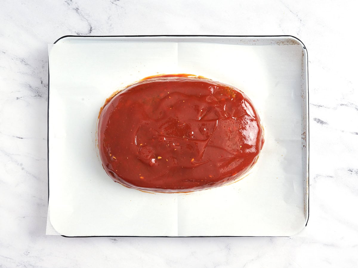 Un pain de viande aux lentilles sur une plaque à pâtisserie tapissée de papier sulfurisé et recouverte de glaçage.