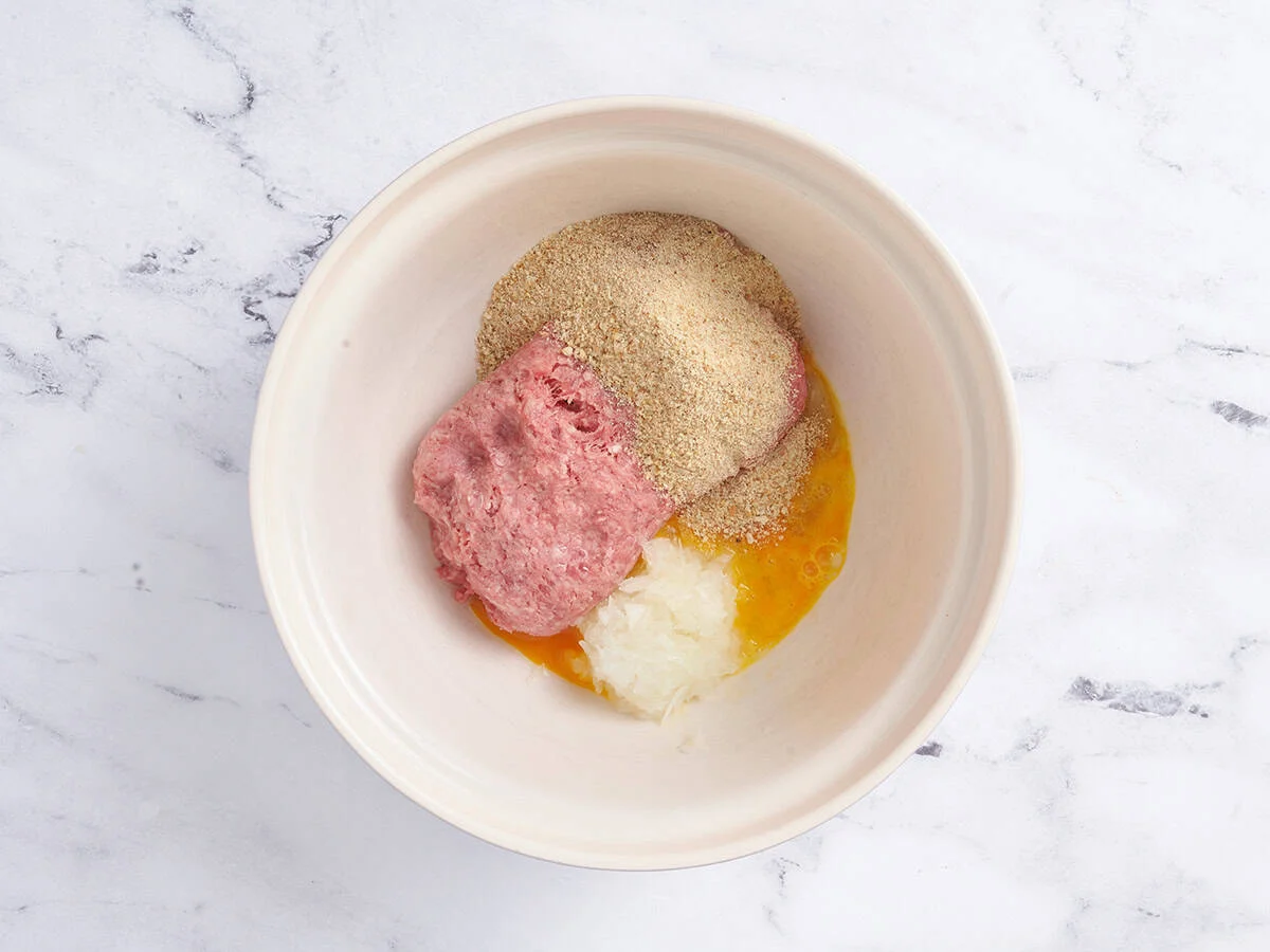 Chapelure, assaisonnements et viande hachée dans un bol à mélanger.