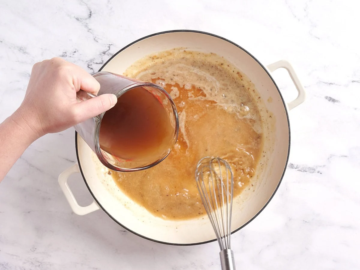Bouillon de boeuf ajouté à un roux dans une casserole.