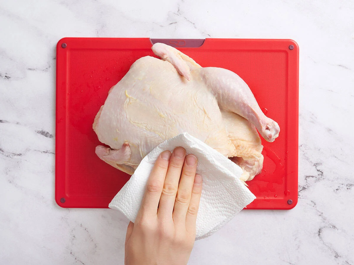 Une main utilisant une serviette en papier pour sécher un poulet entier.