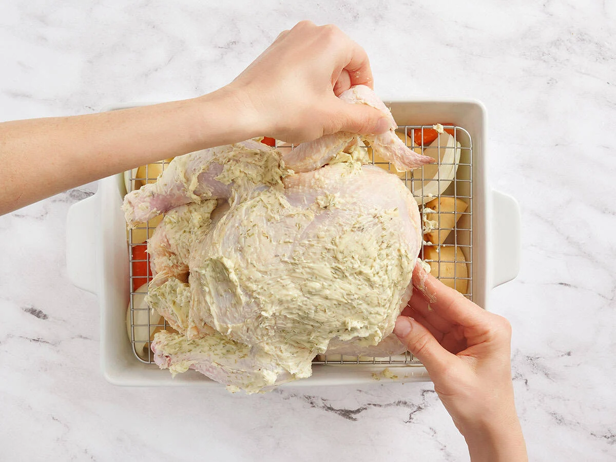 Mains rentrant les ailes de poulet sous un poulet entier.