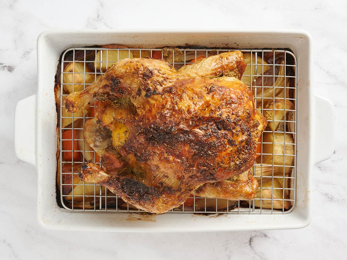 Poulet rôti dans un plat allant au four posé sur des légumes.