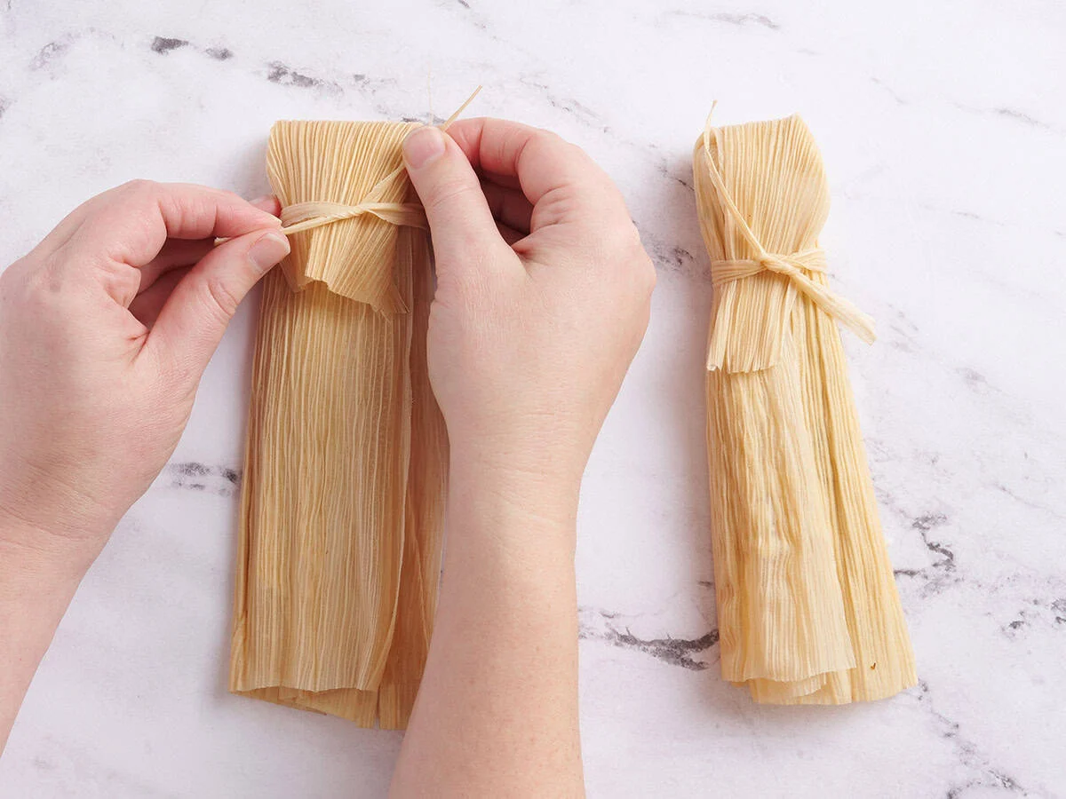 Mains faisant un nœud autour d’une balle de maïs remplie.