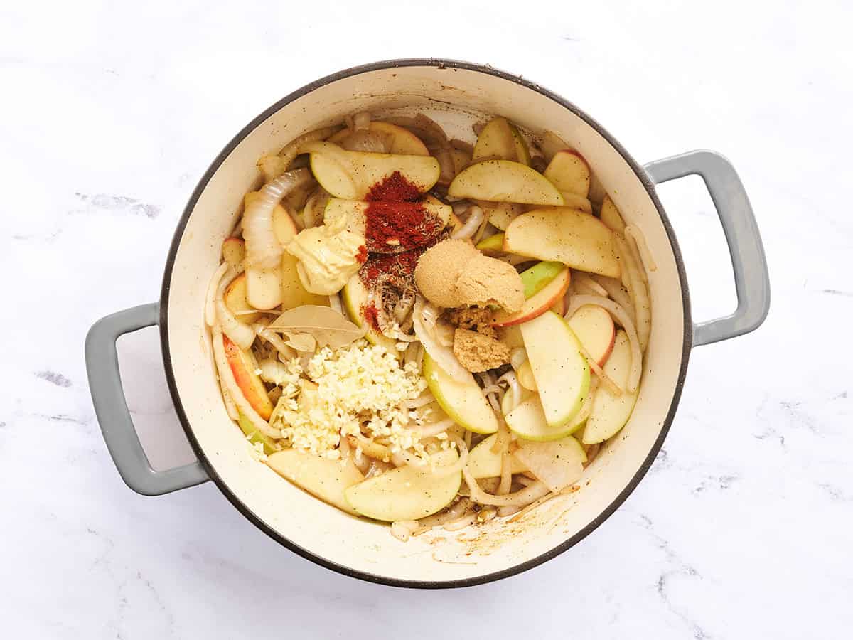 Épices ajoutées à une cocotte d'oignons et de pommes.