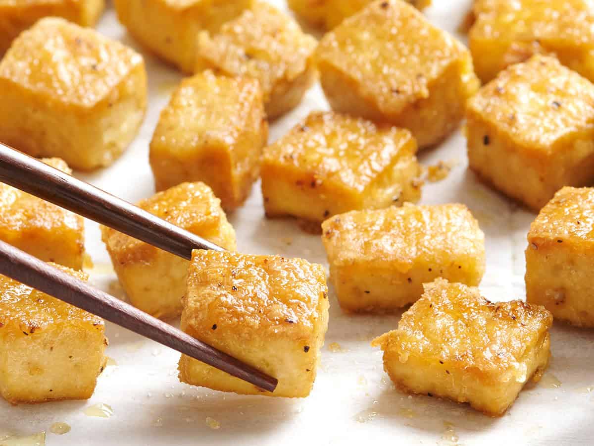 Overed view of baked tofu being picked up with chopsticks.