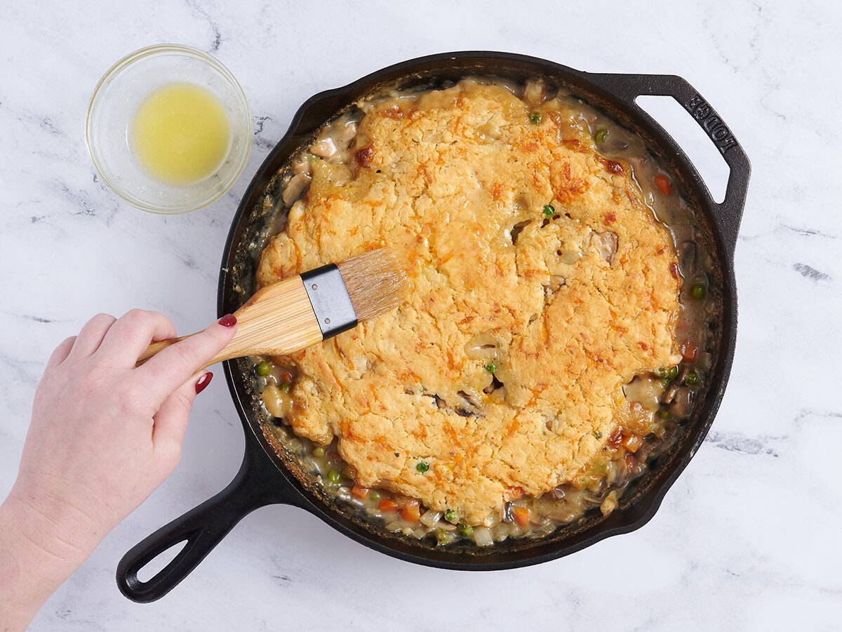 Une main badigeonnant du beurre fondu sur un cordonnier de poulet.