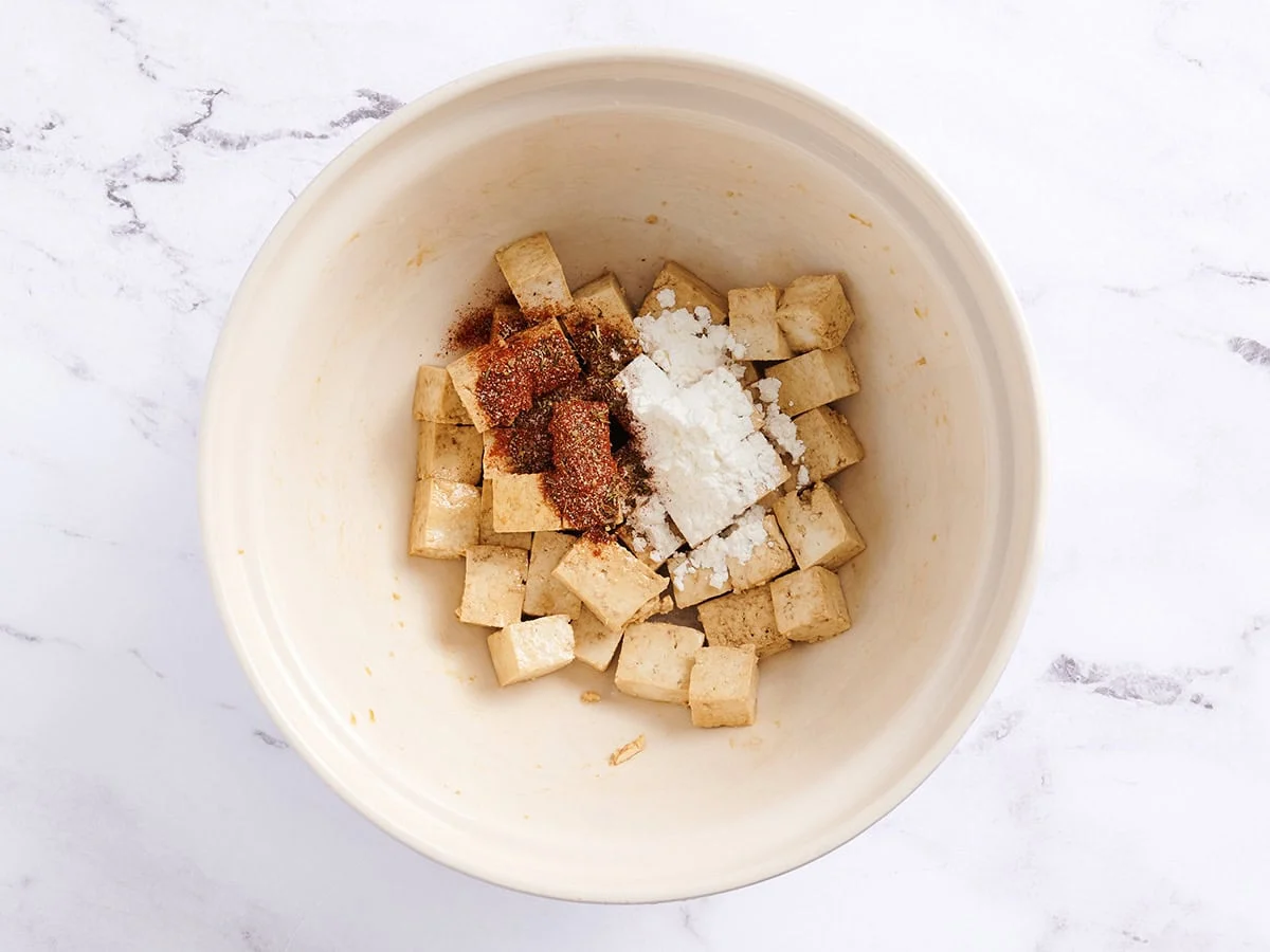 Tofu en cubes avec fécule de maïs et assaisonnement cajun dans un bol blanc. 