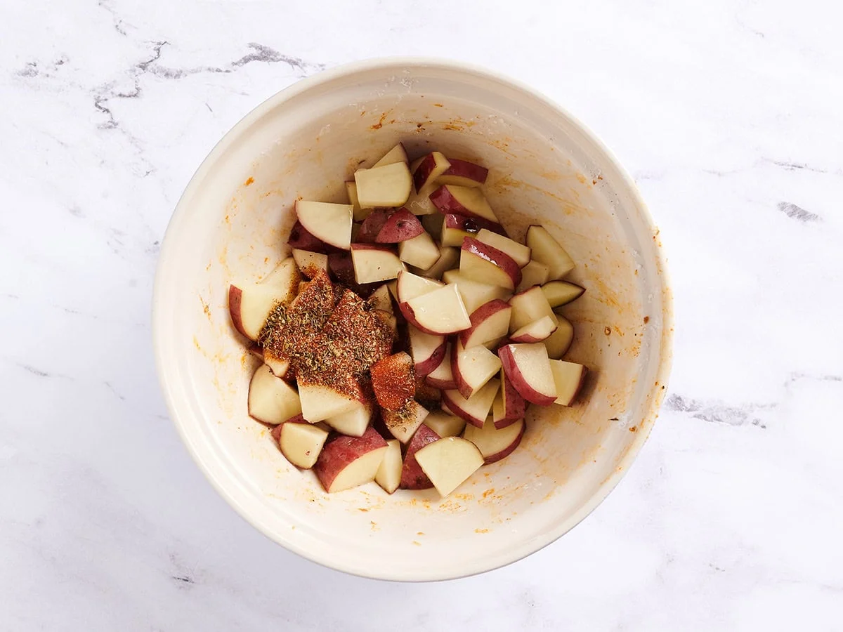 Pommes de terre en cubes avec assaisonnement cajun dans un bol blanc. 